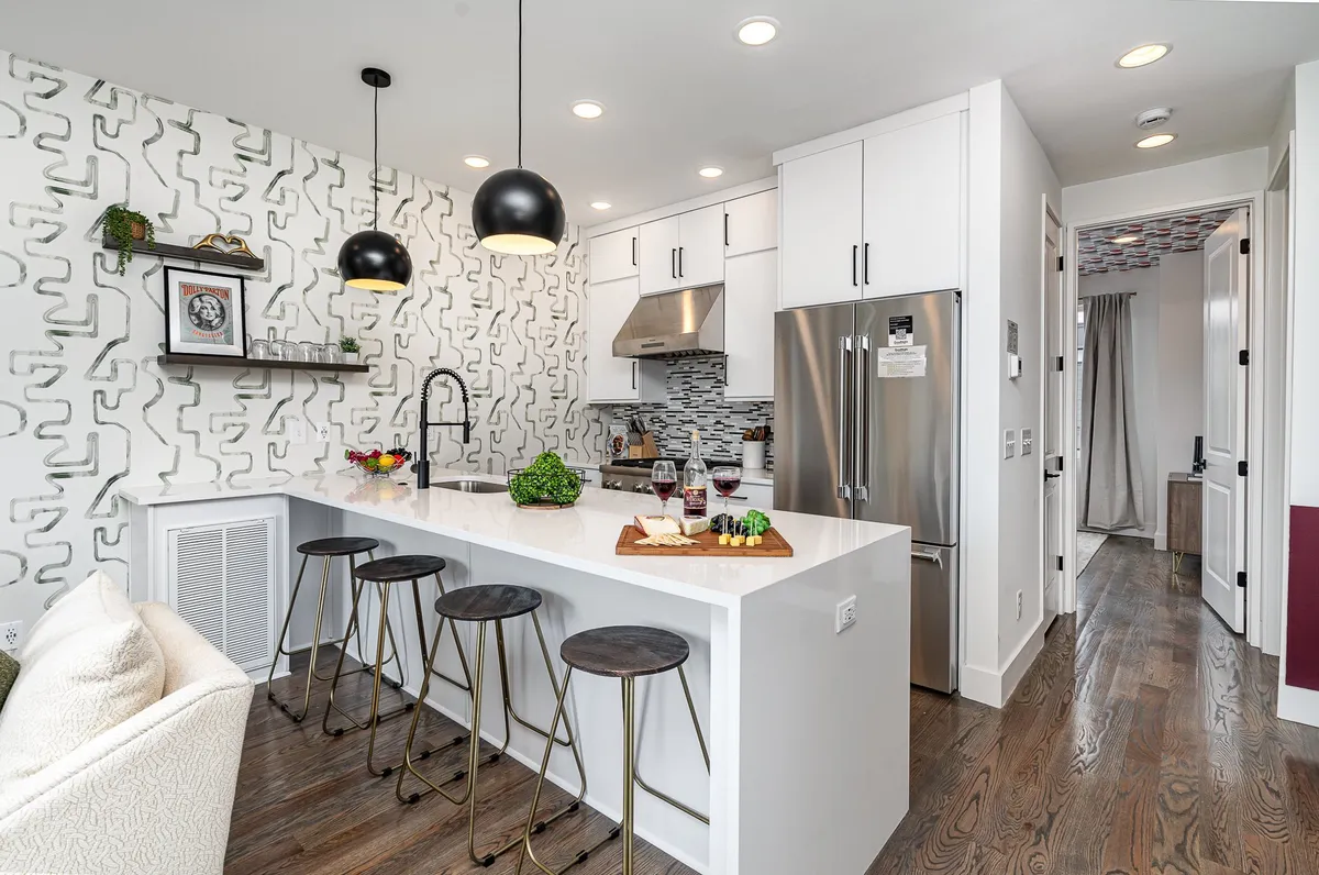 A contemporary kitchen with a central island, modern pendant lights, and a decorative wall. A charcuterie board and wine glasses hint at social gatherings, while sleek appliances and bar seating emphasize the kitchen's modern amenities and open layout.