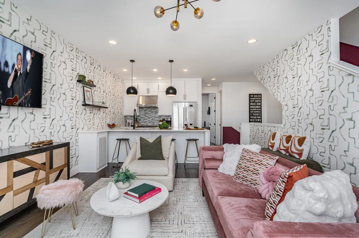 The image showcases a spacious, stylish open-concept living area with a cozy sofa, chic coffee table, modern kitchen island, vibrant wall art, and a large television. The space is designed for both relaxation and entertaining, with inviting seating for game nights, a fully-equipped kitchen for group meals, and an airy, contemporary vibe.