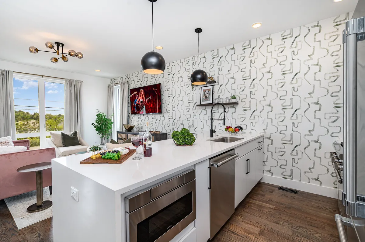 A stylish, modern kitchen with a central island, pendant lights, and decorative wallpaper, complemented by a window that brings in natural light. The scene invites you to imagine cooking, dining, or enjoying a relaxed gathering.