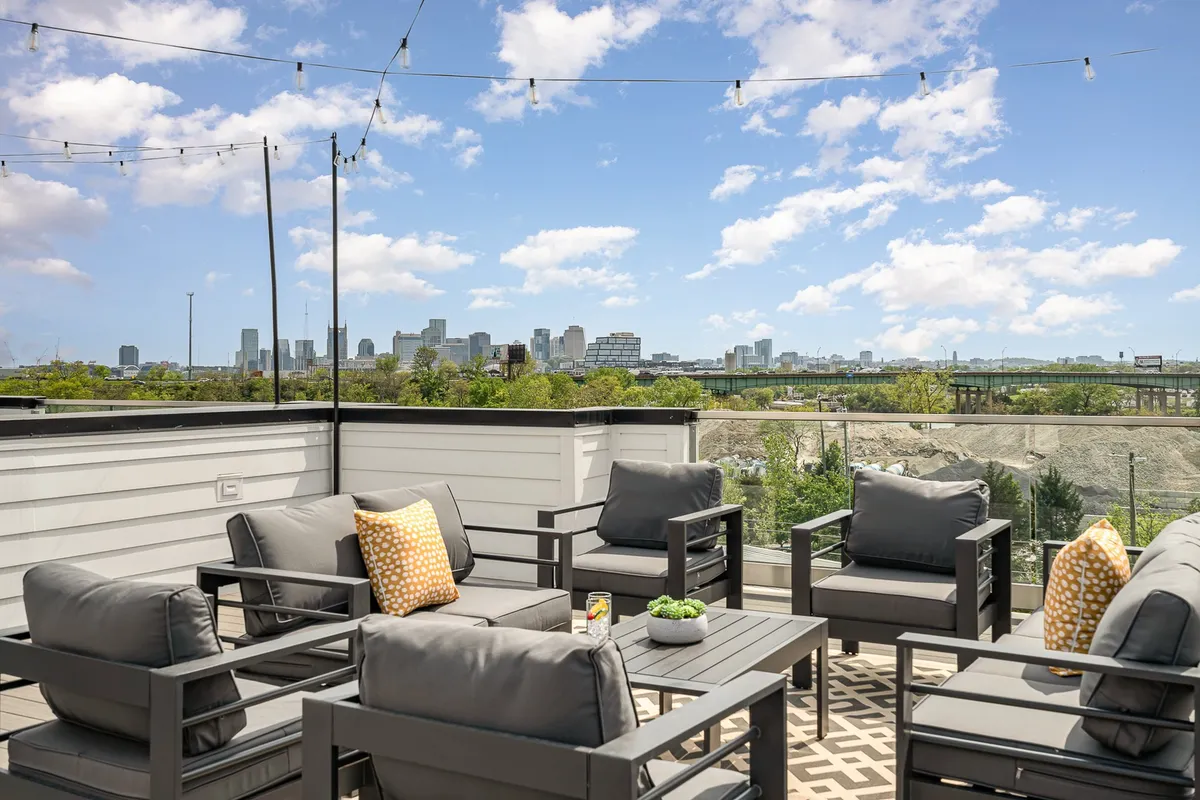 A stylish outdoor seating area with decorative pillows, twinkling string lights, and stunning city skyline views. Guests are pictured enjoying sunset moments and the vibrant city lights, creating an atmosphere of casual social gatherings and outdoor entertaining.