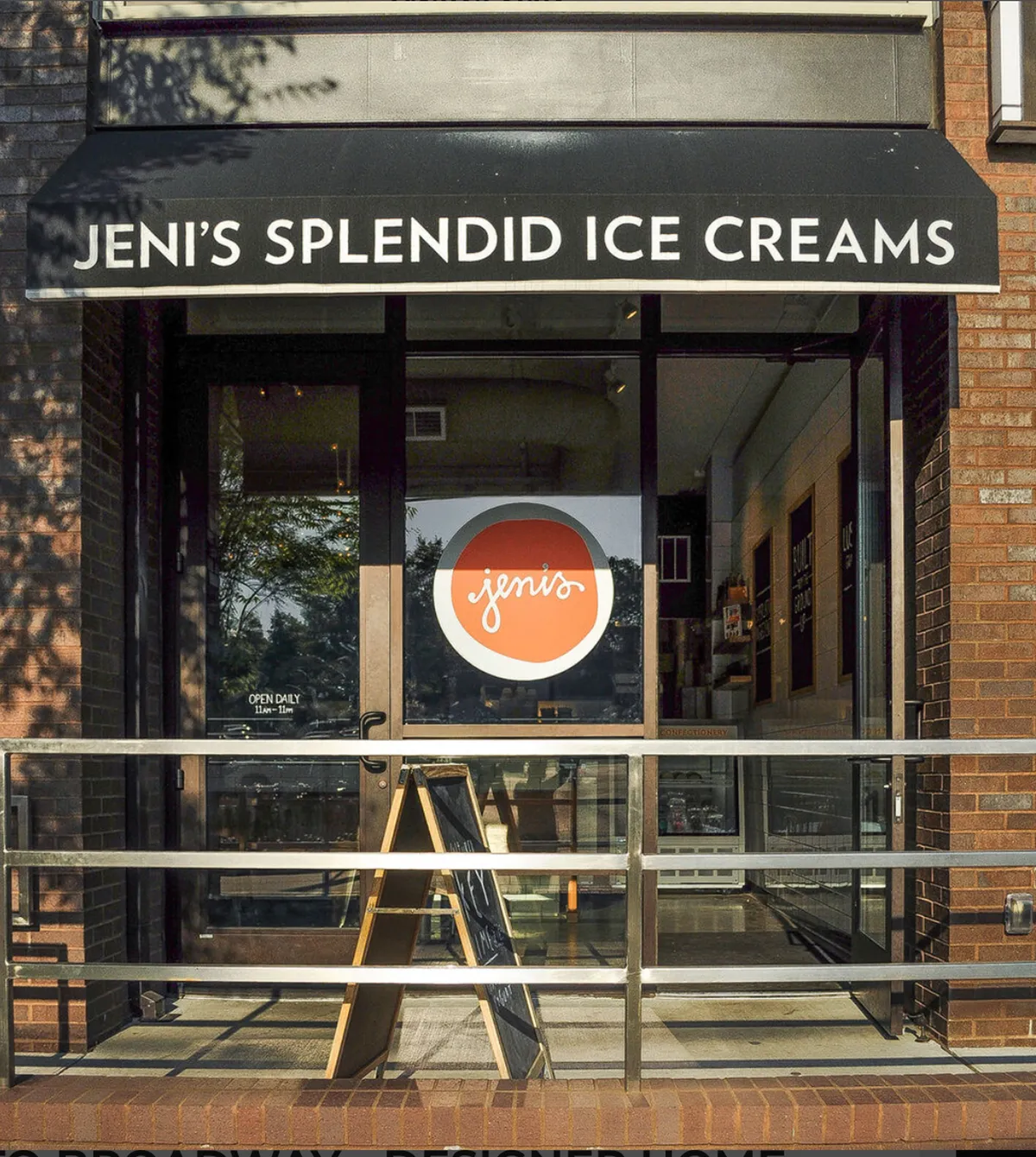 The image shows the cheerful storefront of an ice cream shop, with an open door and a menu board inviting visitors to step inside. The outdoor seating area is welcoming, hinting at a relaxed neighborhood vibe and the promise of delicious treats for families and kids.