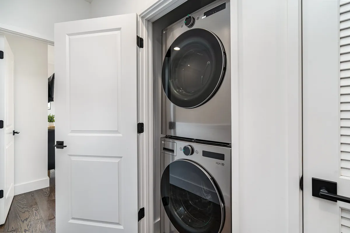 A clean, efficient laundry area featuring a stacked washer and dryer set against white cabinetry. The space is well-organized, with a doorway leading to another room, suggesting easy access and integration within the home.