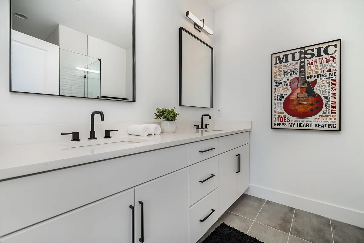 A contemporary bathroom with double vanity sinks, mirrors, and music-themed artwork. The space is fresh and modern, designed for comfort and convenience.